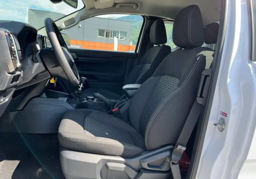 Vue intérieure côté conducteur du Ford Ranger 2025 blanc, montrant sièges tissu noirs et tableau de bord avec volant multifonctions.