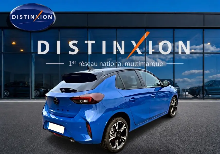 Opel Corsa 1.2 turbo bleu en 3/4 arrière droit, avec jantes alu et toit noir devant une vitrine Distinxion.