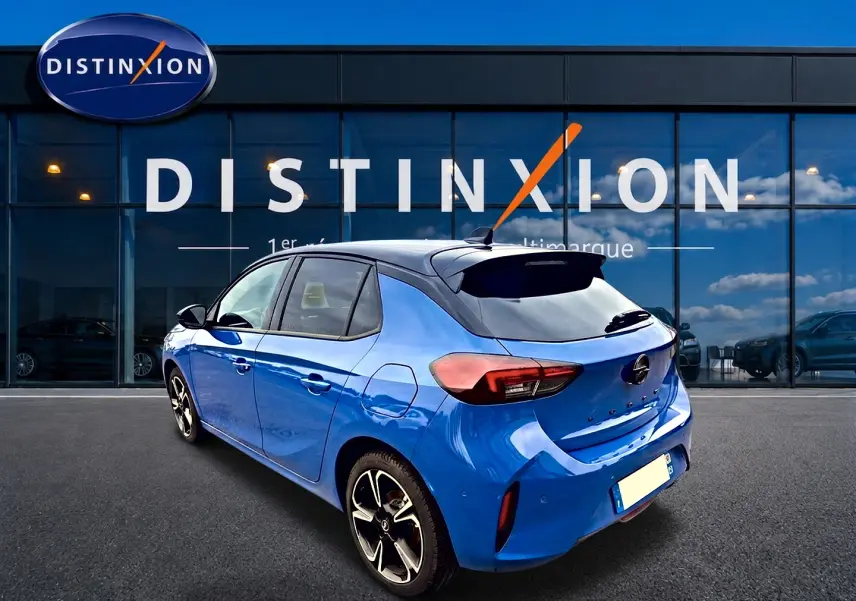 Opel Corsa bleu 3/4 arrière droit avec toit noir et jantes alliage devant showroom Distinxion.