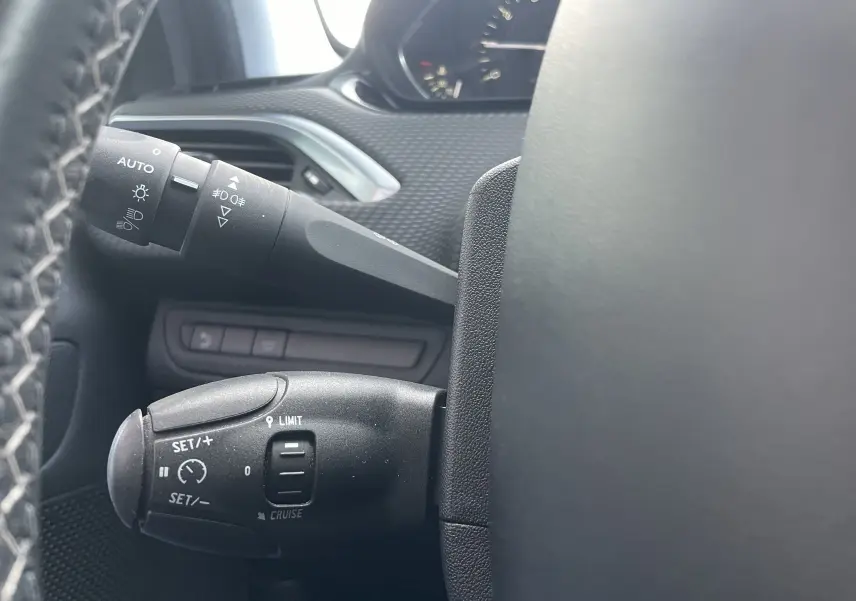 Gros plan sur les commandes de régulateur et des phares à gauche du volant d'un Peugeot 2008 gris, intérieur noir.