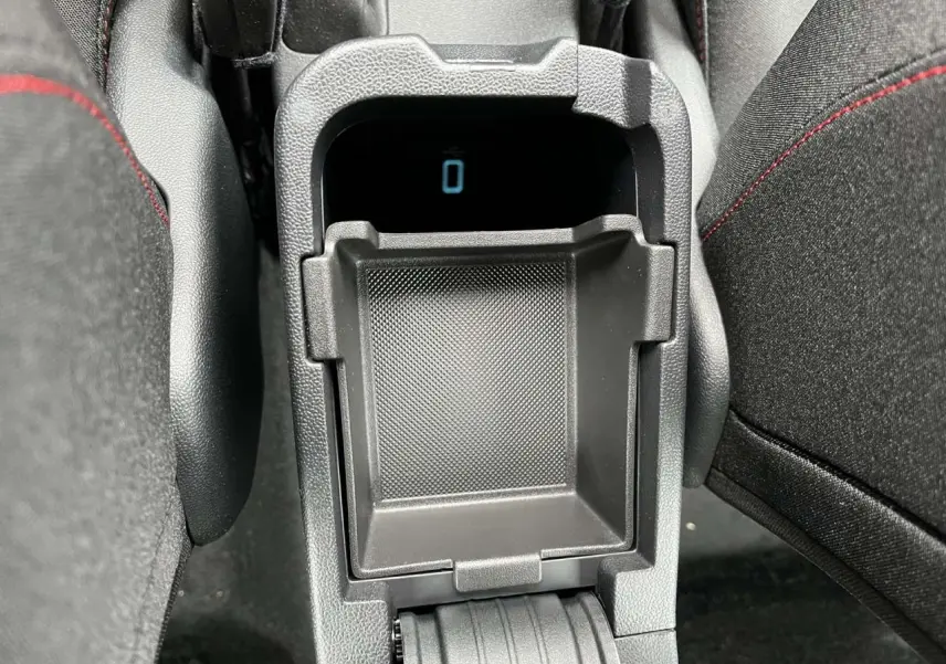 Gros plan sur la console centrale noire du Ford Puma 2023, montrant un rangement ouvert entre les sièges noirs avec surpiqûres rouges.