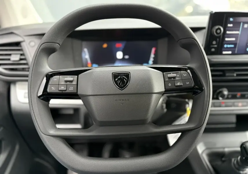 Vue rapprochée du volant noir du Peugeot Expert Fourgon 2025 avec commandes intégrées et tableau de bord numérique flou.