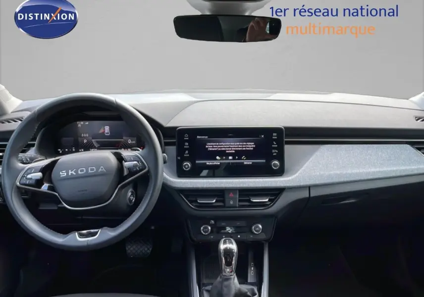 Intérieur de la Skoda Scala 2025 en vue frontale, tableau de bord gris/noir avec écran tactile central et volant multifonction.