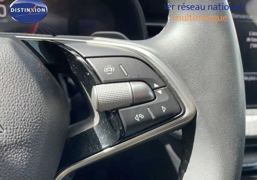 Gros plan sur les commandes multifonctions en plastique noir et chrome du volant gris d'une Skoda Scala blanche.