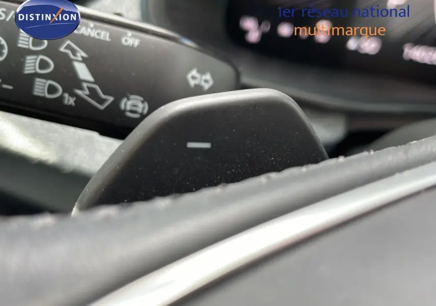 Détail du levier de commande au volant d'une Skoda Scala blanc glacier, avec affichage numérique flou en arrière-plan.