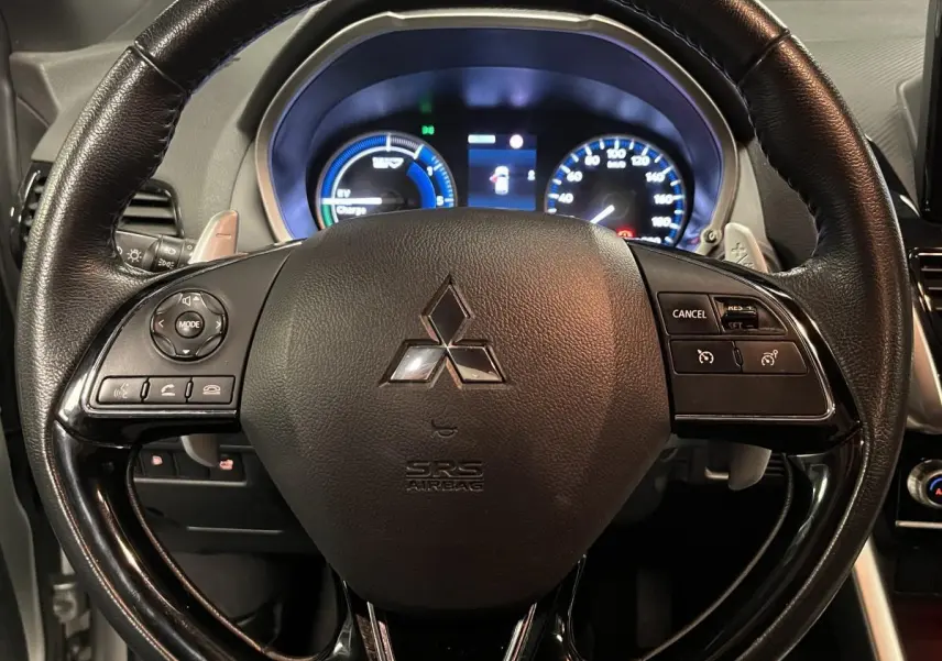 Volant en cuir noir du Mitsubishi Eclipse Cross 2022 avec commandes intégrées et tableau de bord éclairé en arrière-plan.