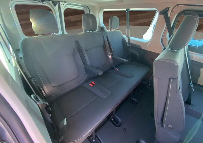 Vue intérieure arrière du Renault Trafic Combi 2025 gris Highland, sièges tissu noir avec ceintures et accoudoirs visibles.