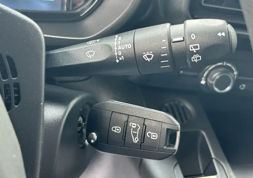 Gros plan sur la clé de contact insérée et la commande d'essuie-glace dans l'habitacle d'un Citroën Berlingo Fourgon blanc.