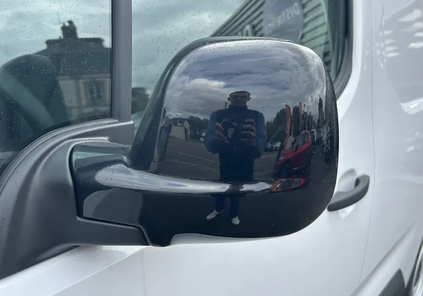 Rétroviseur noir côté gauche du Citroën Berlingo Fourgon blanc, avec reflet d'un photographe en extérieur.