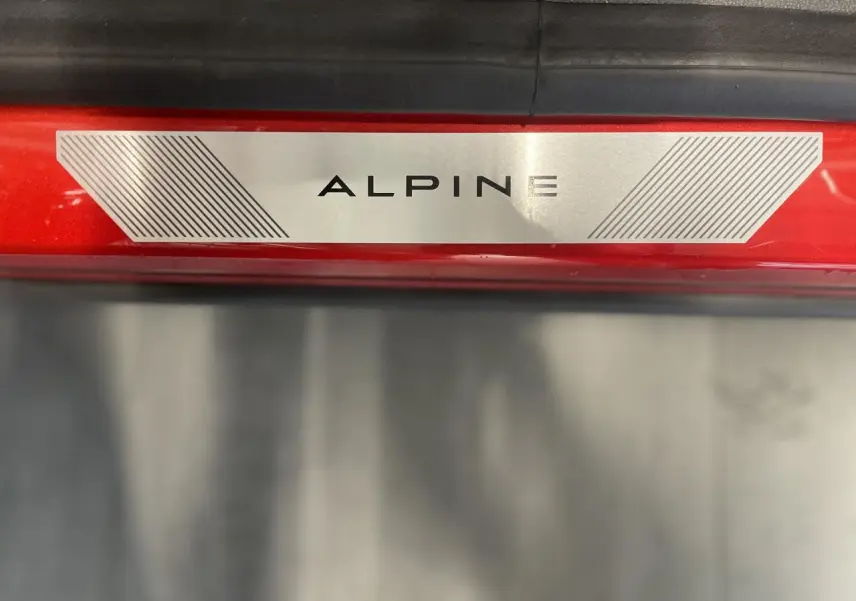 Gros plan sur la plaque de seuil de porte "ALPINE" sur la carrosserie rouge métallisée du Renault Austral.
