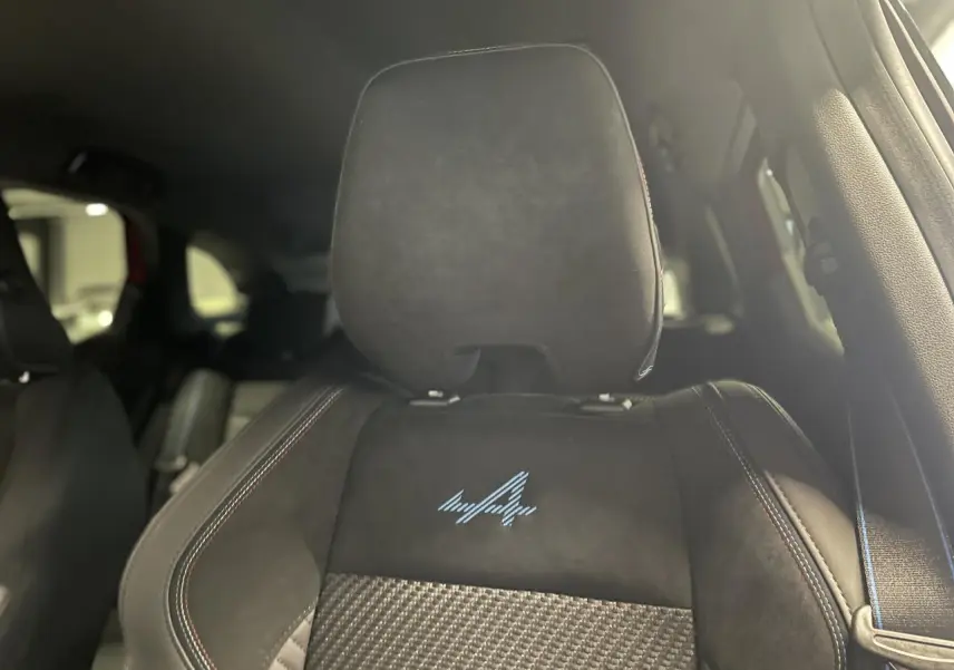 Gros plan sur le siège avant en Alcantara noir avec logo Alpine bleu et surpiqûres tricolores du Renault Austral.