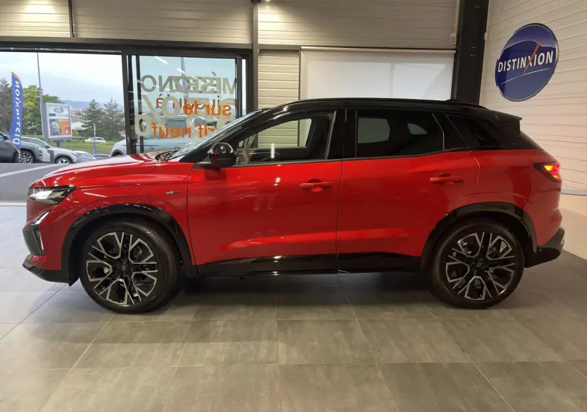 Profil gauche du Renault Austral 2025 rouge métallisé avec toit noir et jantes alliage 20 pouces en intérieur showroom.