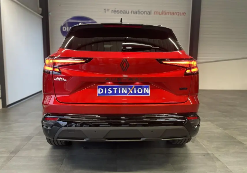 Vue arrière du Renault Austral rouge métallisé avec toit noir, feux LED allumés et logo noir brillant distinctif.