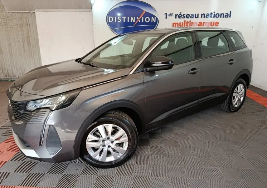 Peugeot 5008 gris clair vue 3/4 avant droit, avec jantes alliage et feux LED dans un showroom intérieur.