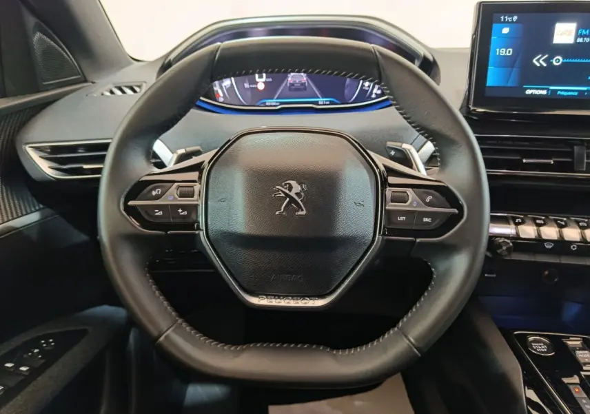 Vue rapprochée du volant cuir multifonctions noir du Peugeot 5008 2023 avec tableau de bord digital et écran tactile.