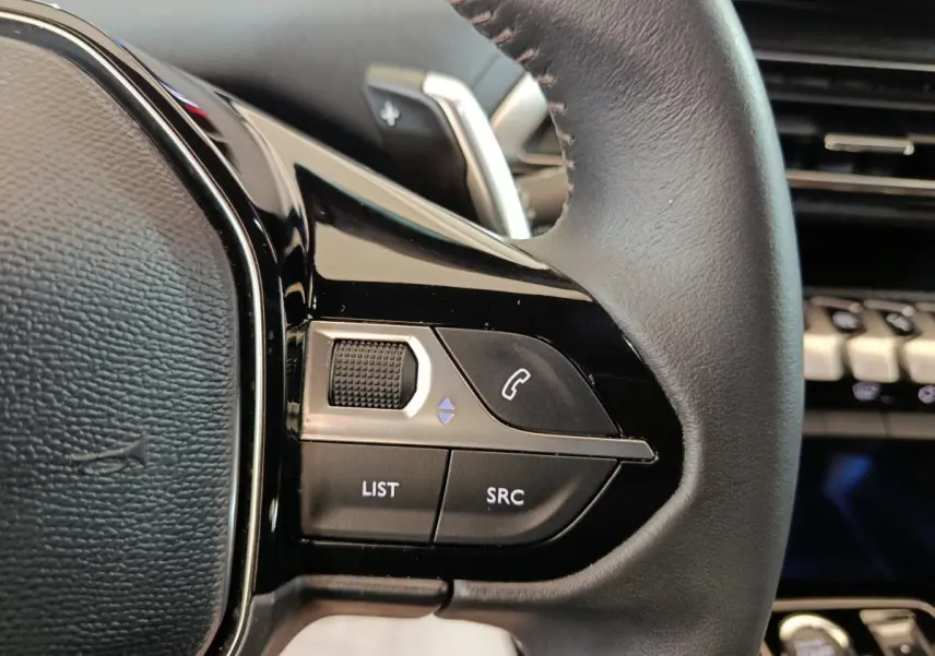 Gros plan sur le volant cuir noir multifonctions de la Peugeot 5008 2023, avec commandes audio et téléphone intégrées.