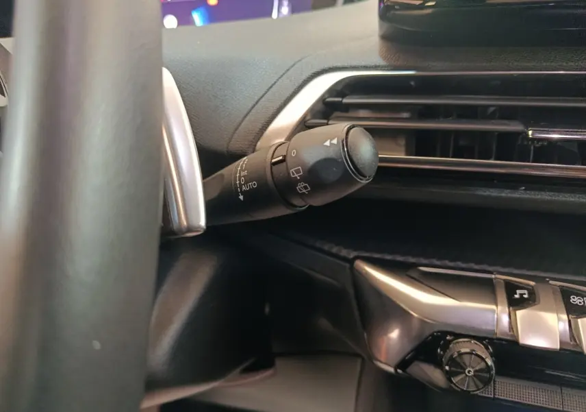 Gros plan sur la commande d’essuie-glace à gauche du volant cuir dans l’habitacle noir du Peugeot 5008 gris clair 2023.