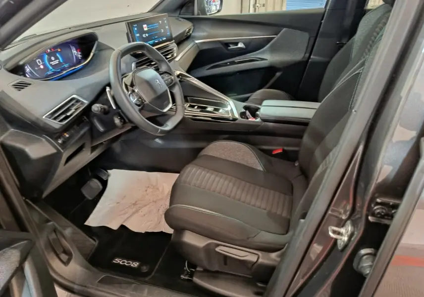 Vue intérieure côté conducteur du Peugeot 5008 gris clair 2023, avec volant cuir multifonctions et tableau de bord digital.