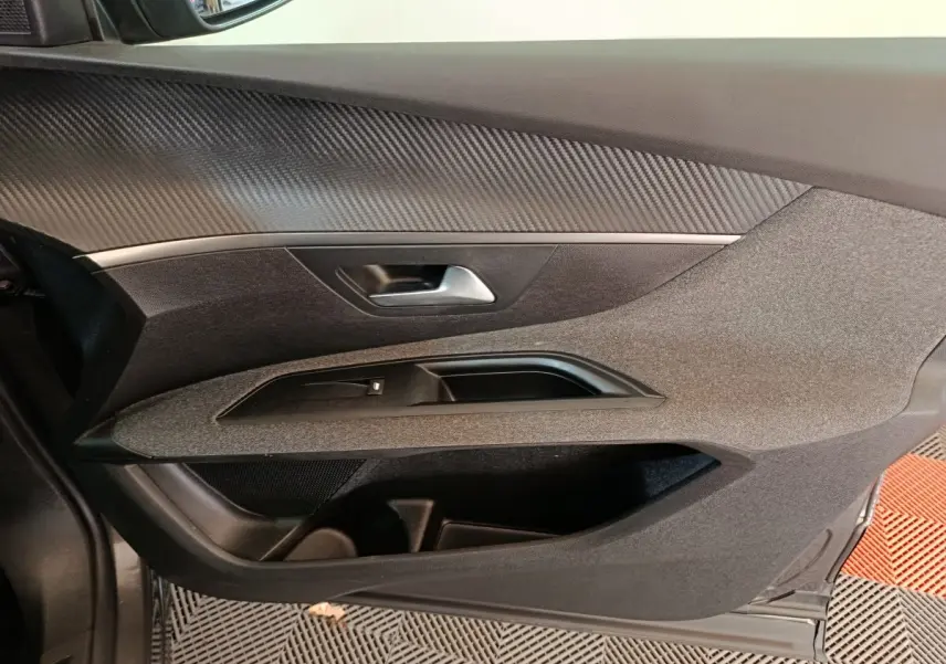 Gros plan sur la porte intérieure côté gauche du Peugeot 5008 gris clair, avec garniture textile et poignée argentée.