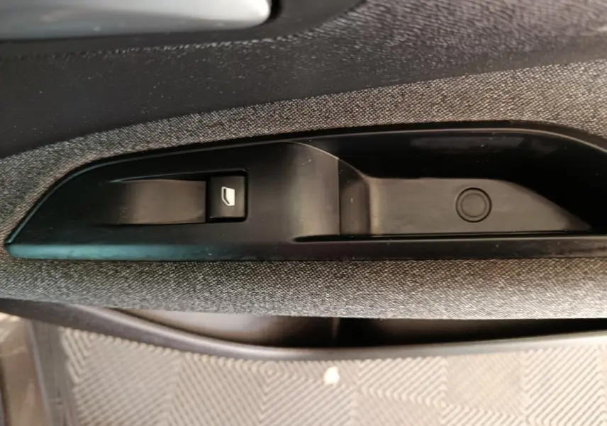 Gros plan sur la commande de lève-vitre noire intégrée à la garniture grise de la porte côté conducteur du Peugeot 5008 gris clair.