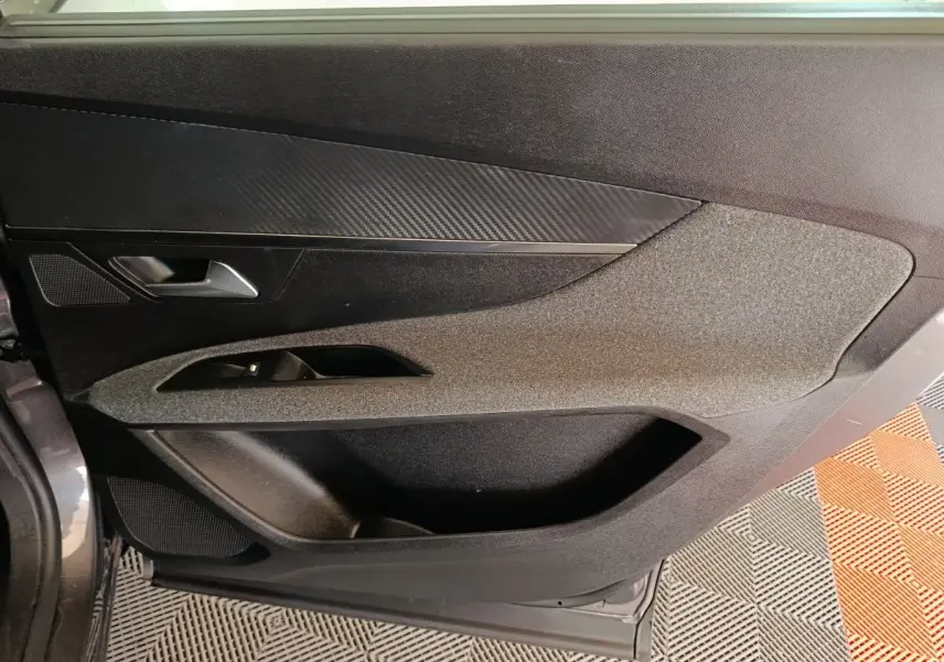 Vue intérieure du panneau de porte avant gauche gris foncé du Peugeot 5008 2023 avec insert effet carbone et commande de vitre.
