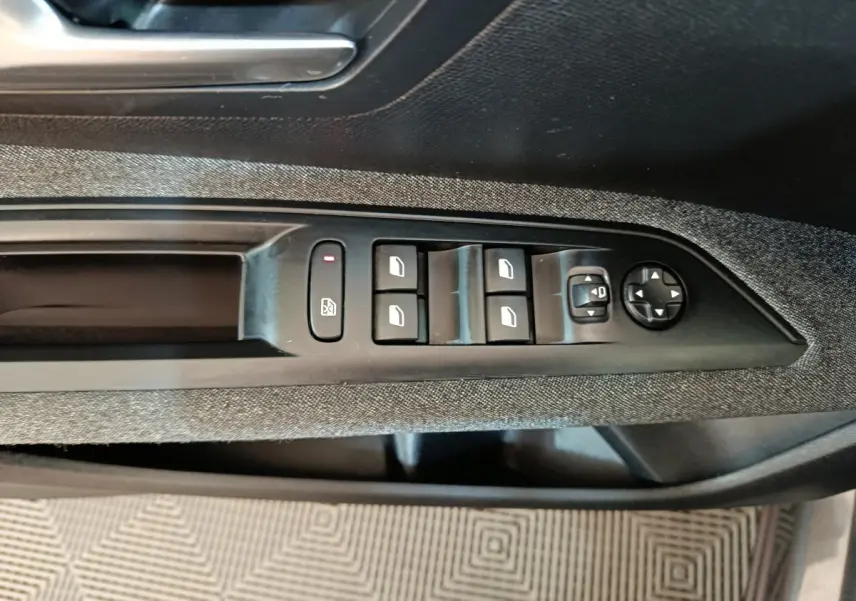 Gros plan sur les commandes de lève-vitres et rétroviseurs côté conducteur du Peugeot 5008 gris clair 2023.