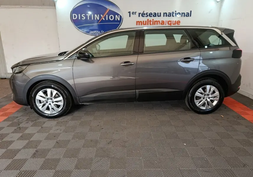 Vue de profil côté gauche d’un Peugeot 5008 gris clair de 2023, SUV familial avec jantes alliage et toit noir.
