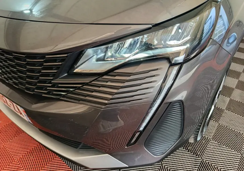 Gros plan sur l’avant droit gris clair du Peugeot 5008 2023, mettant en valeur le phare LED et la calandre distinctive.