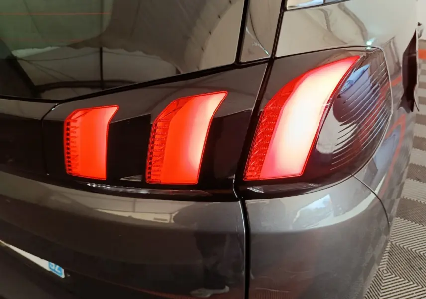 Gros plan sur le feu arrière droit rouge d’un Peugeot 5008 gris clair, avec reflet du plafond sur la carrosserie.