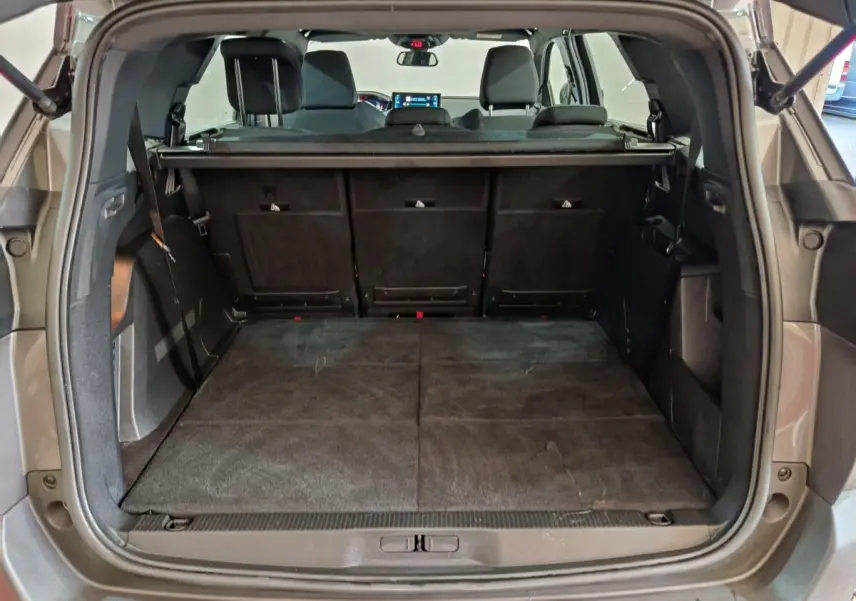 Vue arrière du coffre ouvert d'un Peugeot 5008 gris clair 2023 avec banquette arrière rabattue et tablette de coffre visible.