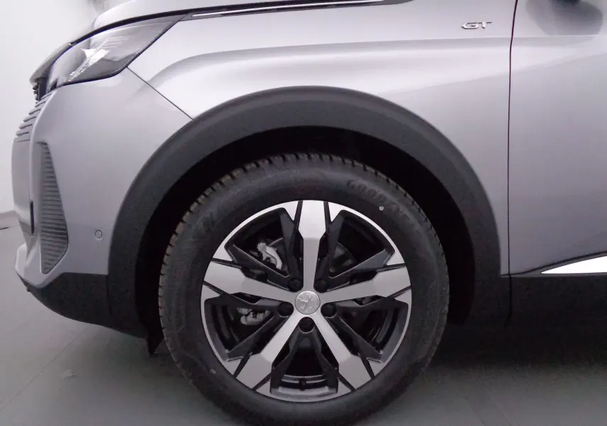 Gros plan sur la roue avant gauche du Peugeot 3008 gris Artense Métal avec jante alliage bicolore et badge GT visible.