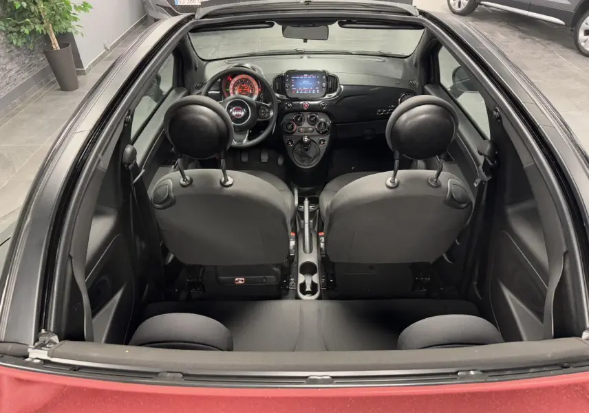 Vue intérieure arrière du cabriolet Fiat 500 noir avec capote rouge, volant noir et tableau de bord moderne.