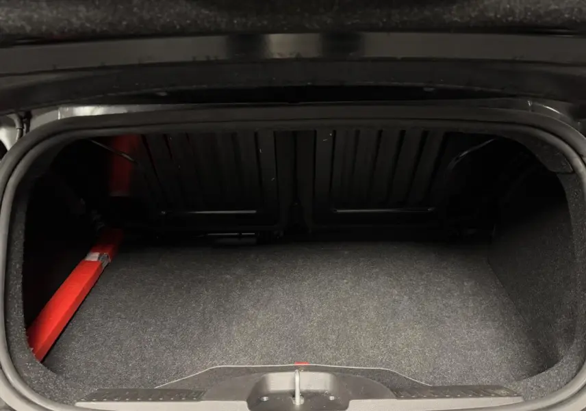 Coffre ouvert de la Fiat 500 Cabriolet noire, montrant l'espace de rangement et la capote rouge repliée.