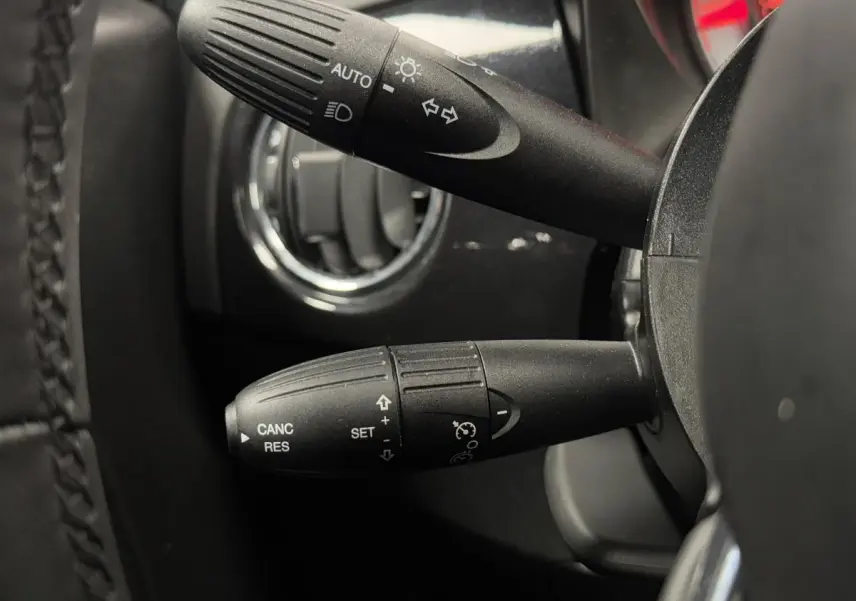 Gros plan sur les commandes au volant noir de la Fiat 500 Cabriolet 2024 avec détails des fonctions d'éclairage et régulateur de vitesse.