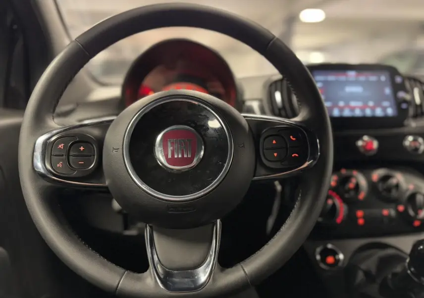 Volant noir en éco-cuir de la Fiat 500 Cabriolet 2024 avec commandes intégrées et tableau de bord flou en arrière-plan