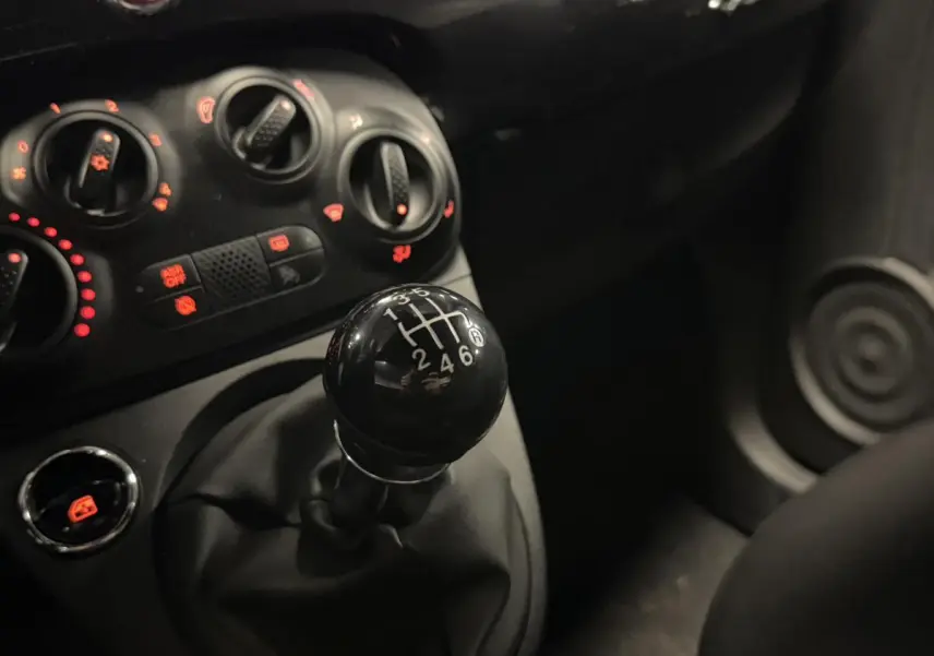 Gros plan sur le levier de vitesses manuel noir et les commandes de climatisation du tableau de bord d'une Fiat 500 Cabriolet noire.