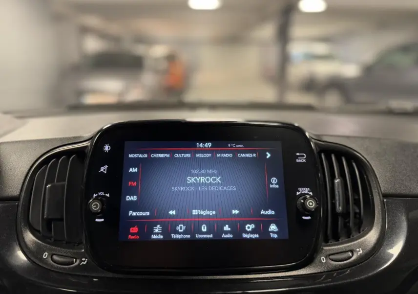 Gros plan sur l'écran tactile central de la Fiat 500 Cabriolet noire, affichant la radio Skyrock en intérieur voiture.