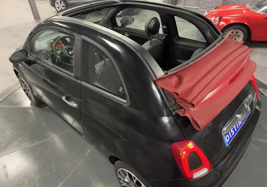 Vue 3/4 arrière droite d'une Fiat 500 Cabriolet noire avec capote rouge partiellement repliée et jantes alliage 16 pouces.