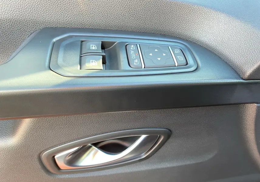 Gros plan sur la commande des vitres et la poignée intérieure côté gauche d'une porte noire du Renault Trafic Combi 2025.