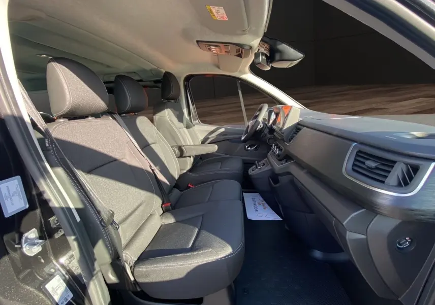 Intérieur avant du Renault Trafic Combi noir 2025, sièges tissu noir avec accoudoirs et tableau de bord moderne.