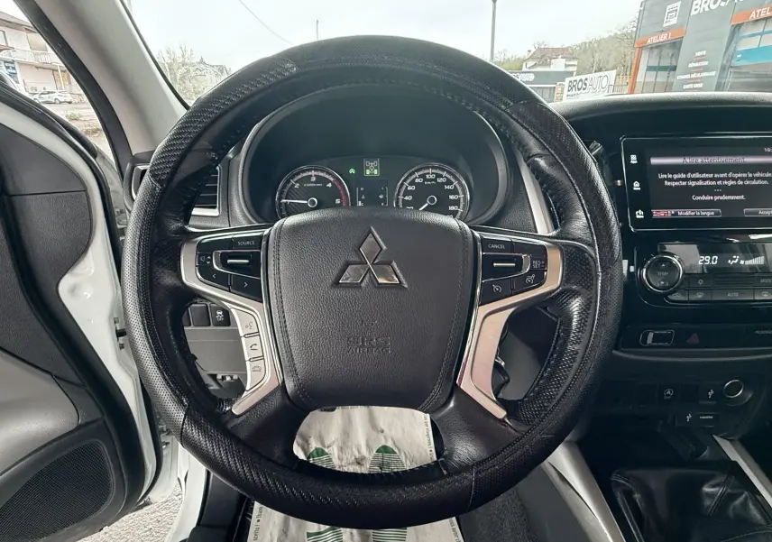 Vue intérieure centrée sur le volant noir du Mitsubishi L200 blanc, avec tableau de bord et écran tactile visibles.