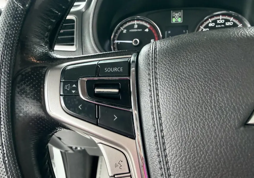 Gros plan sur le volant noir du Mitsubishi L200 Club Cab blanc 2017, avec commandes audio intégrées côté gauche.