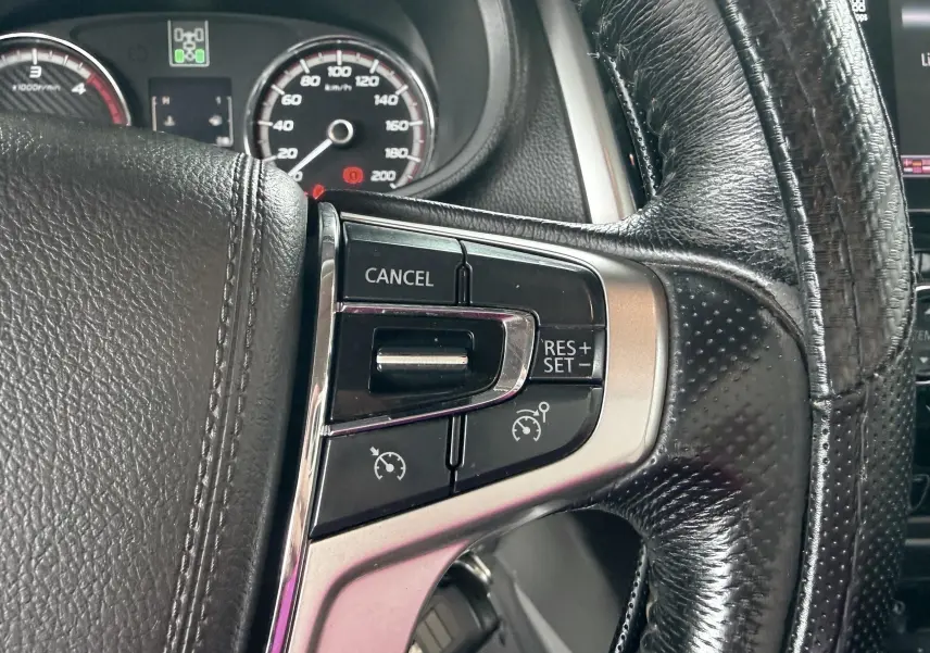Gros plan sur les commandes de régulateur de vitesse au volant cuir du Mitsubishi L200 blanc, tableau de bord en arrière-plan.
