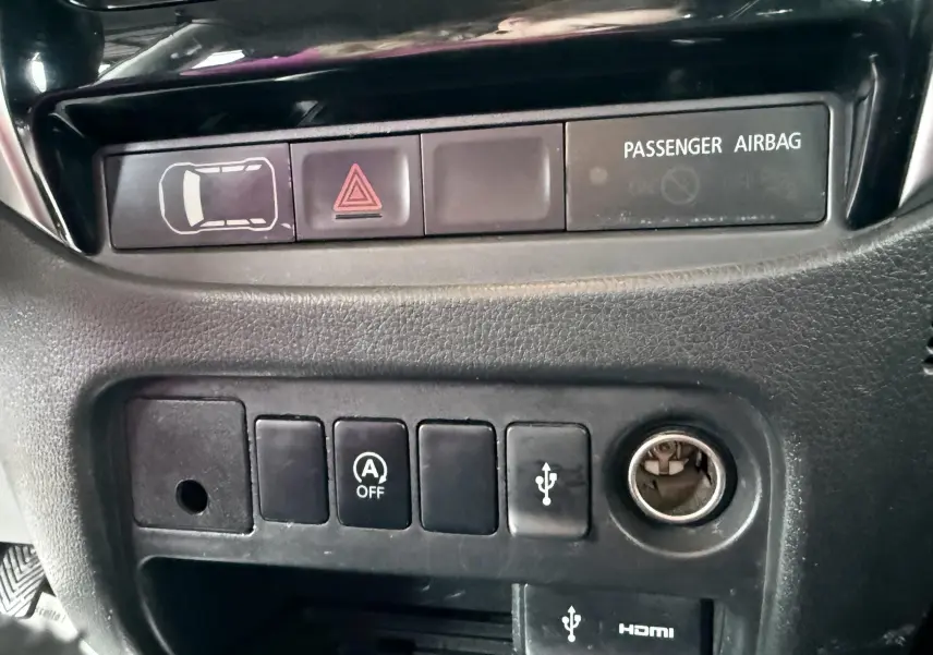 Gros plan sur les commandes du tableau de bord noir du Mitsubishi L200 blanc, avec bouton USB et airbag passager.