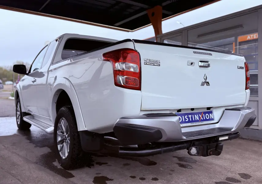 Vue 3/4 arrière droite du pick-up Mitsubishi L200 blanc avec hayon fermé et attelage visible sous le pare-chocs.