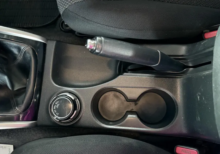 Vue intérieure centrée sur la console centrale du Mitsubishi L200 blanc, montrant frein à main, porte-gobelets et sélecteur 4x4.