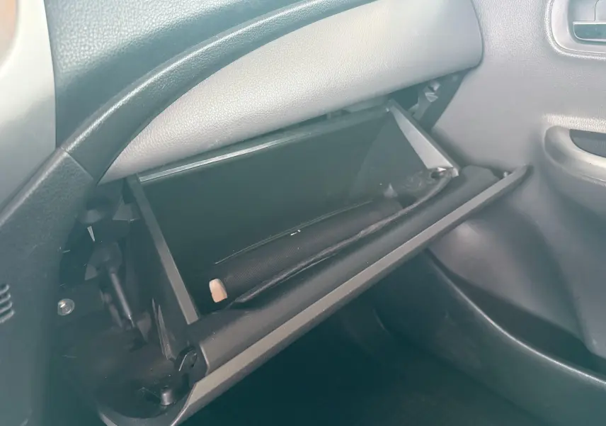 Gros plan sur la boîte à gants ouverte côté passager du Mitsubishi L200 blanc, montrant un rangement intérieur vide.