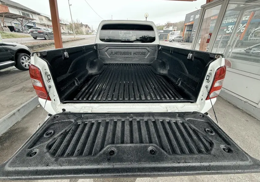 Vue arrière du pick-up Mitsubishi L200 blanc avec la benne ouverte et sa surface de chargement noire texturée.