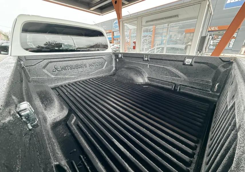 Vue rapprochée de la benne noire texturée du Mitsubishi L200 blanc, avec logo Mitsubishi Motors visible sur la paroi arrière.