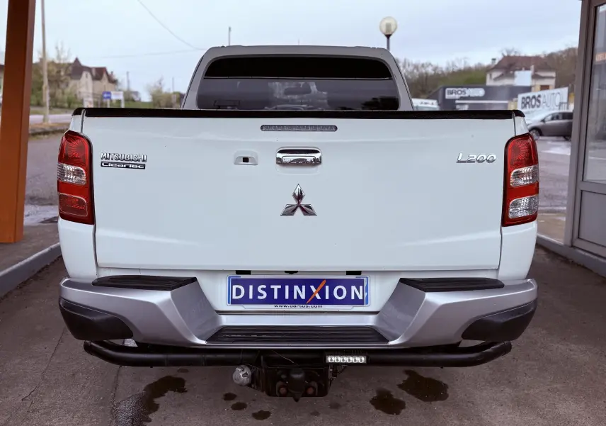 Vue arrière du pick-up Mitsubishi L200 blanc avec hayon fermé et attelage visible sous le pare-chocs.